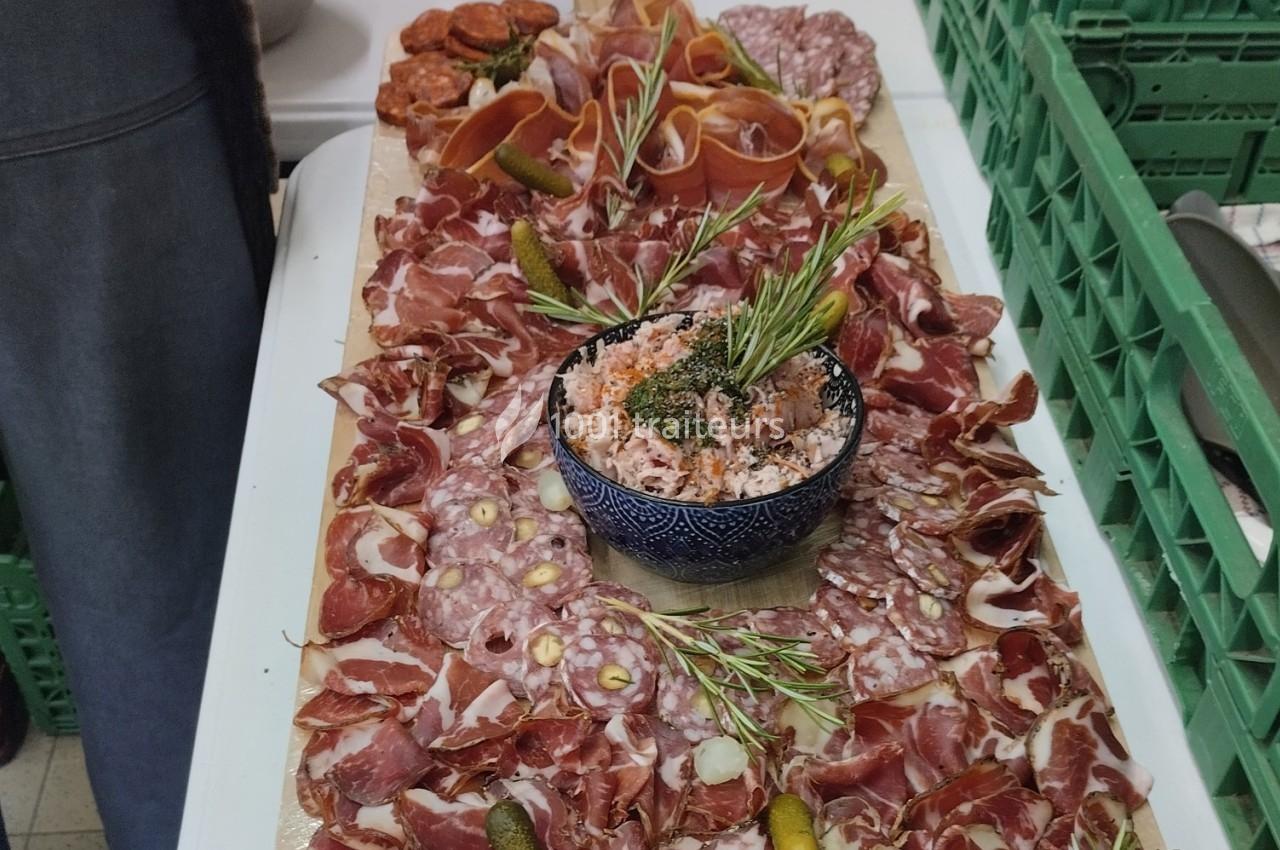 Plateau de charcuterie variée avec jambon, saucisson, cornichons et un bol de rillettes décoré de romarin.