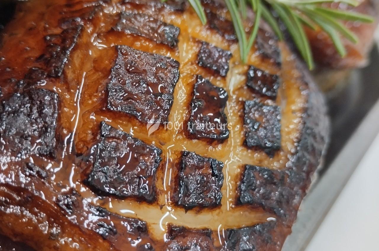 Gros plan d'un rôti caramélisé avec un quadrillage marqué, décoré d'une branche de romarin.