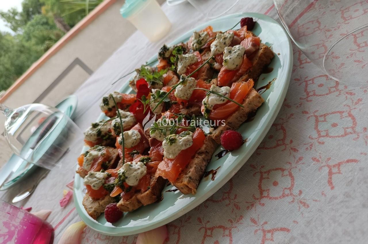 Assiette de toasts garnis de saumon fumé, herbes fraîches et crème, présentée sur une nappe à motifs.