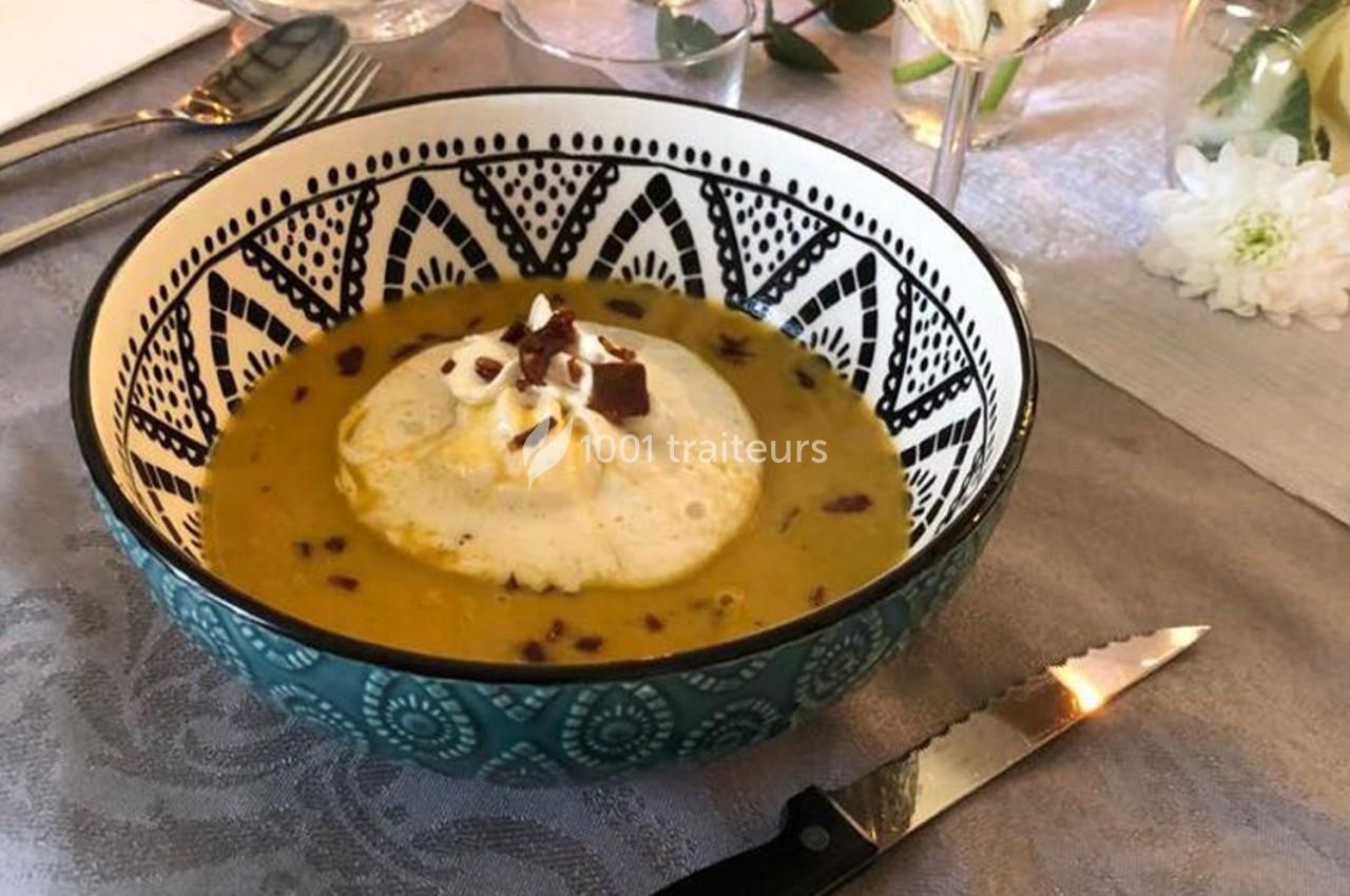 Bol de soupe orangée garnie de crème et éclats de chocolat, posé sur une nappe avec des couverts et décorations.