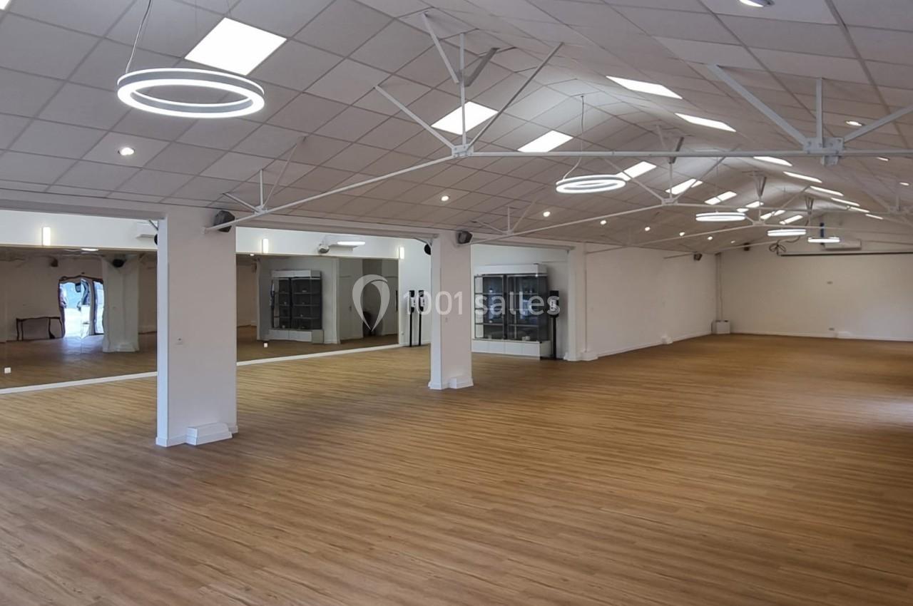 Salle spacieuse avec parquet clair, murs blancs, miroirs et éclairage moderne suspendu.