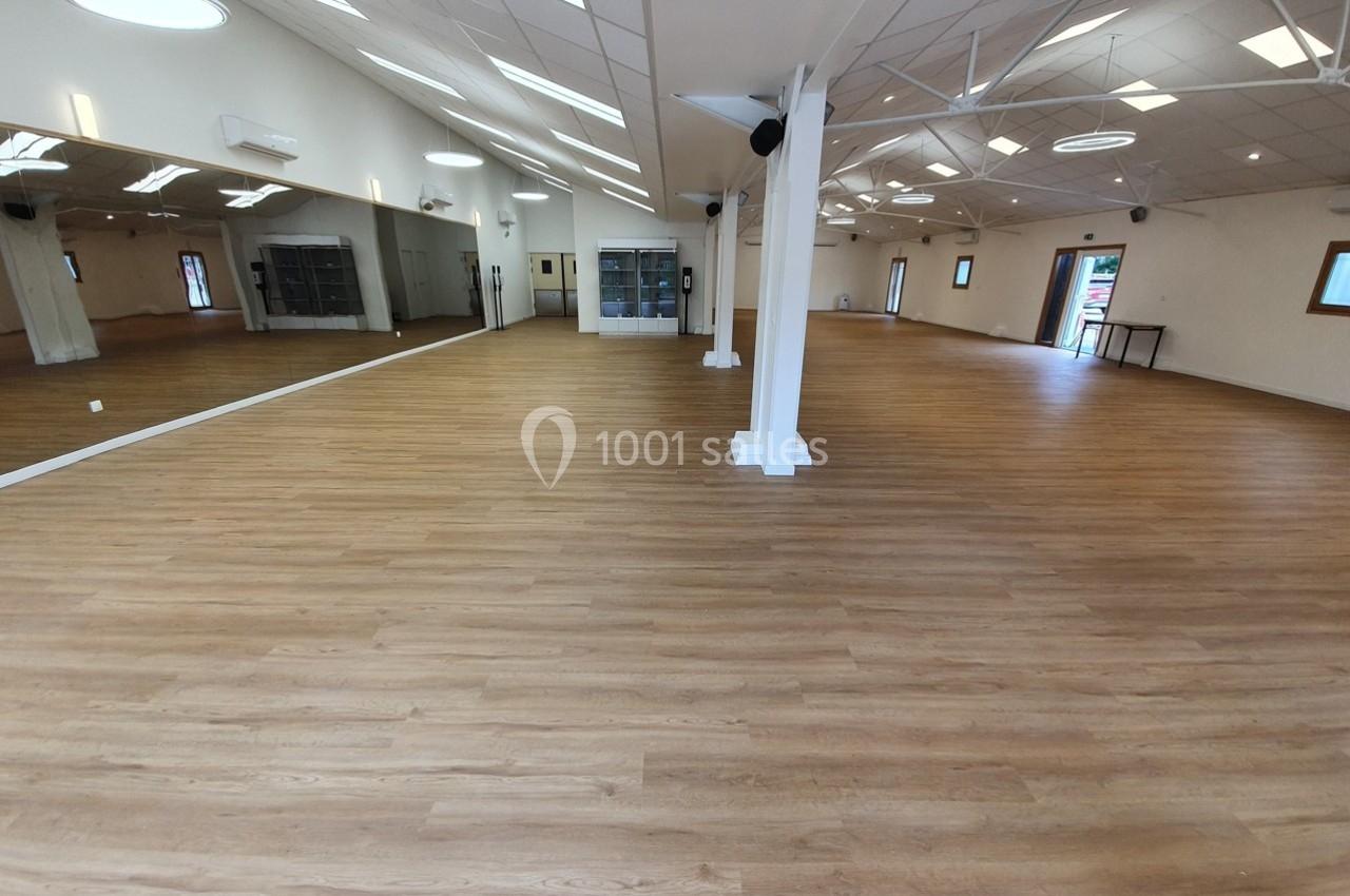 Salle spacieuse avec parquet en bois clair, murs blancs, miroirs et éclairage naturel provenant des fenêtres.