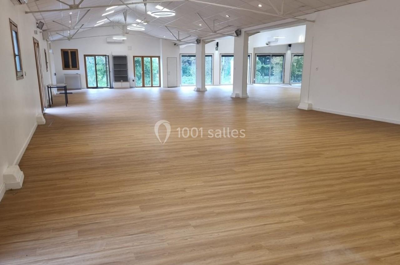 Salle spacieuse avec parquet en bois clair, grandes baies vitrées et plafond blanc avec éclairage moderne.