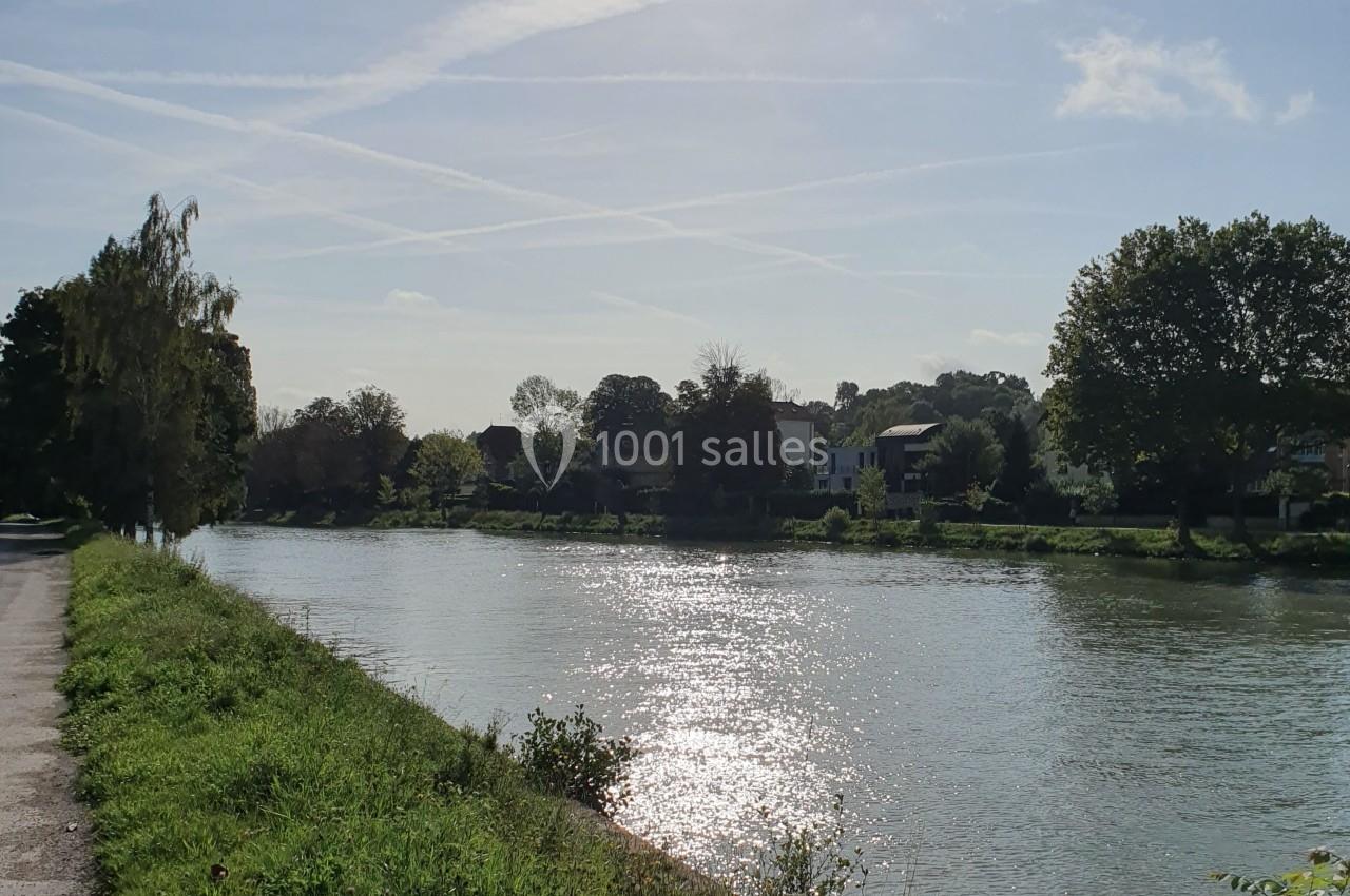 Rivière bordée d'arbres sous un ciel dégagé avec des traînées d'avions, reflet du soleil sur l'eau.