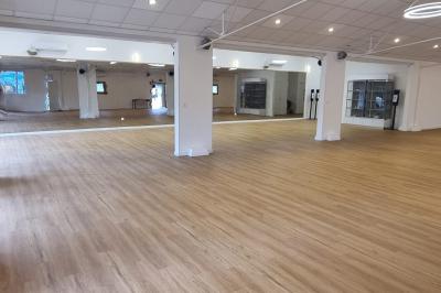 Salle spacieuse avec sol en parquet clair, murs blancs, fenêtres et éclairage suspendu.