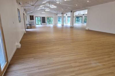 Salle spacieuse avec sol en parquet clair, murs blancs, fenêtres et éclairage suspendu.