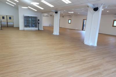 Salle spacieuse avec sol en parquet clair, murs blancs, fenêtres et éclairage suspendu.