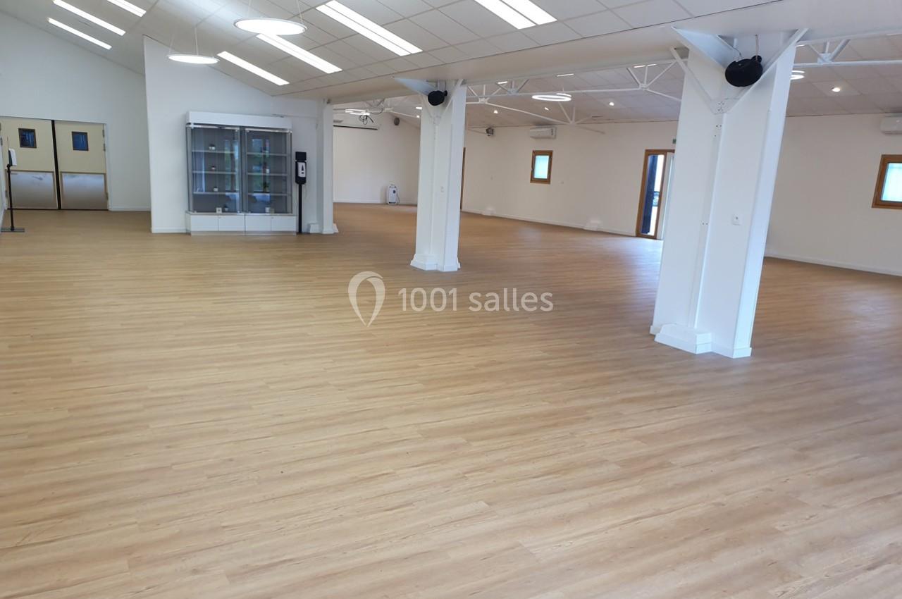 Salle spacieuse avec sol en parquet clair, murs blancs, fenêtres et éclairage suspendu.