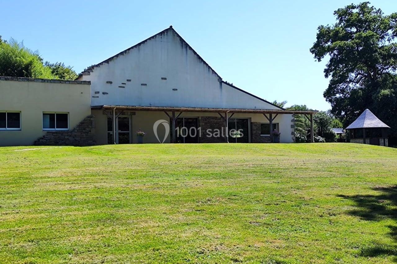Bâtiment avec façade blanche et toit incliné, entouré d'une pelouse verte et d'arbres sous un ciel dégagé.