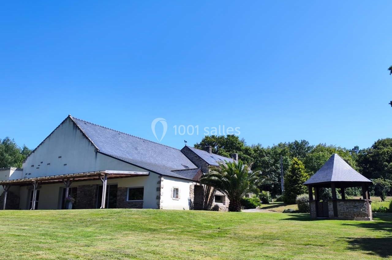 Bâtiment avec toit en ardoise entouré d'un grand jardin verdoyant et d'une petite structure en bois.