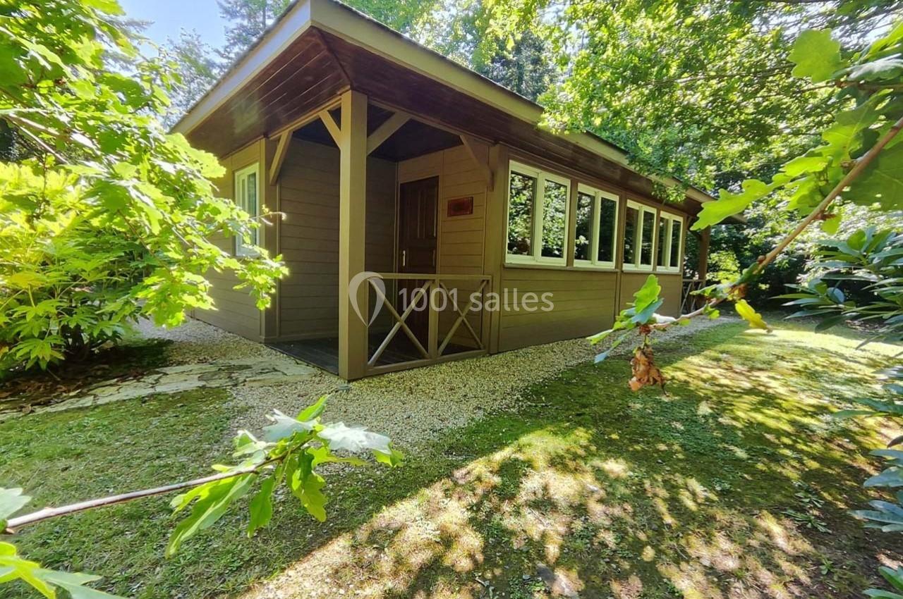Chalet en bois entouré de végétation, avec une allée en gravier et des arbres offrant de l'ombre.
