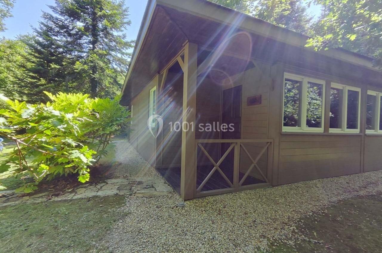 Chalet en bois entouré de végétation, avec une allée de gravier et des rayons de soleil traversant les arbres.