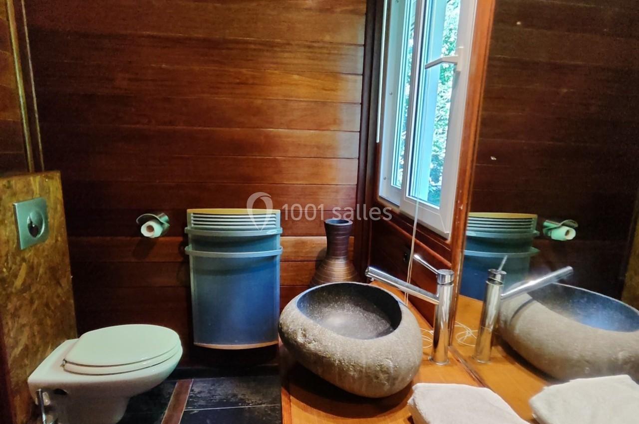 Salle de bain avec murs en bois, lavabo en pierre, toilettes, miroir, fenêtre et accessoires modernes.