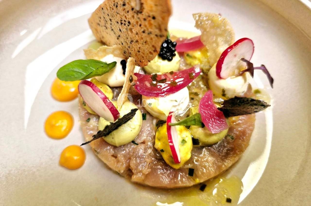 Plat gastronomique composé de tartare, crème, radis, herbes fraîches, gouttes de sauce jaune et chips croustillante.