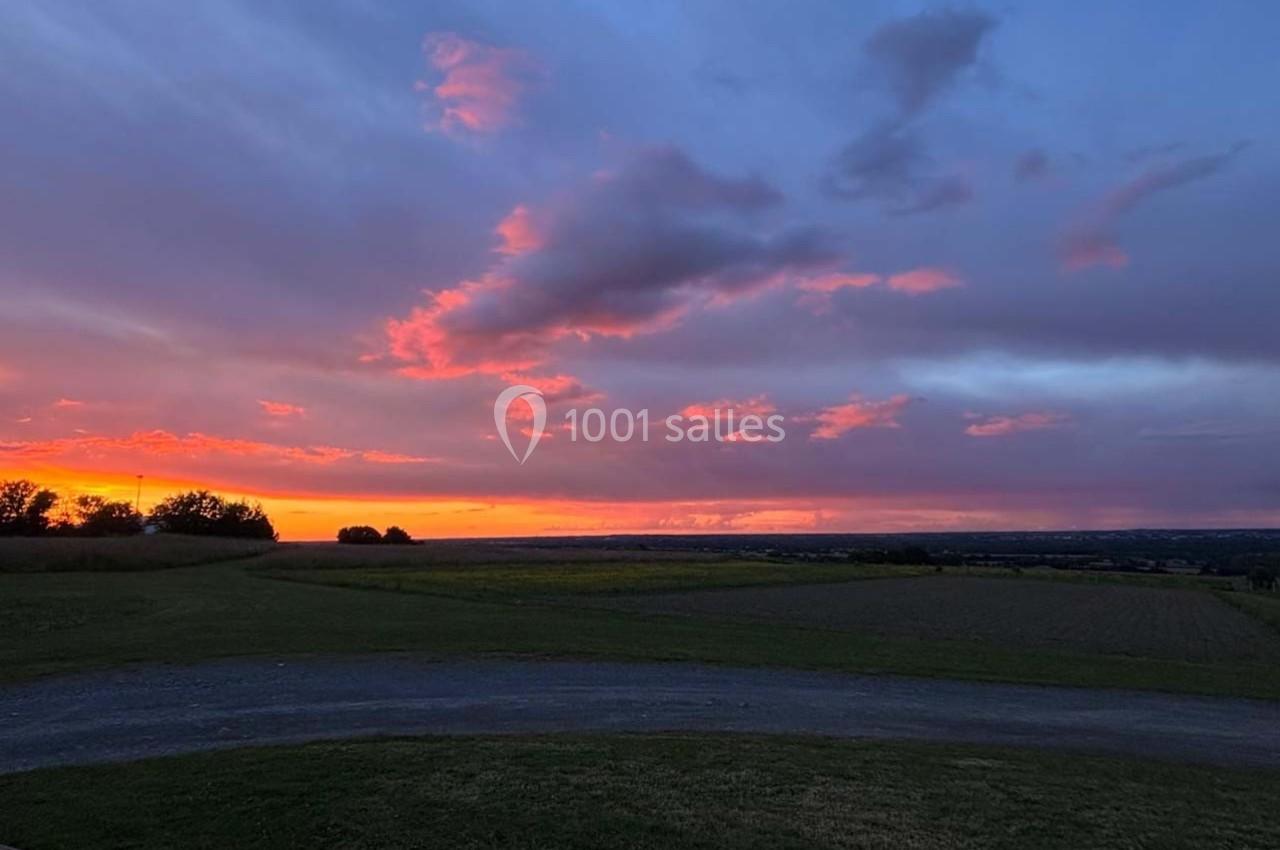 Ciel aux nuances de rose et orange au coucher du soleil, surplombant un paysage de champs et d'arbres.
