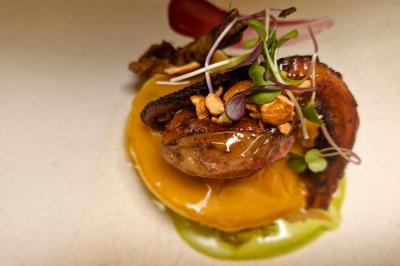 Plat gastronomique composé de viande, légumes, champignons, sauce caramélisée et croustillant sur une assiette décorative.