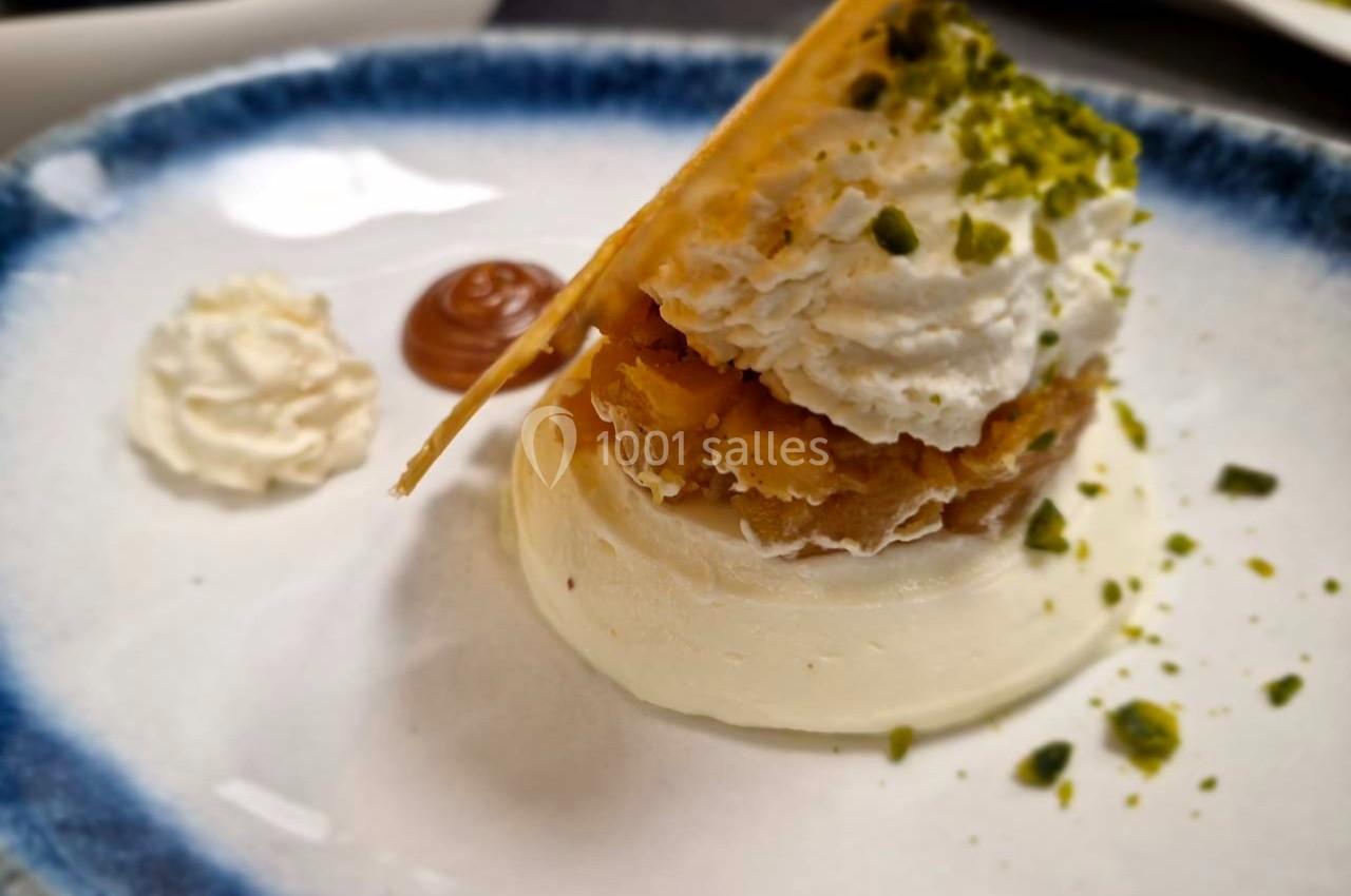 Dessert composé de crème, pâte croustillante, chantilly, éclats de pistache et décorations en sauce sur une assiette.