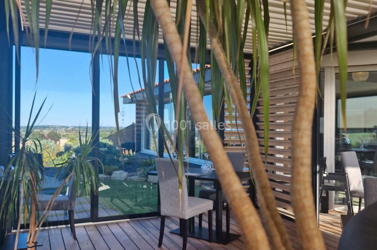 Salle à manger lumineuse avec grandes baies vitrées, plantes en premier plan et vue sur un jardin extérieur.