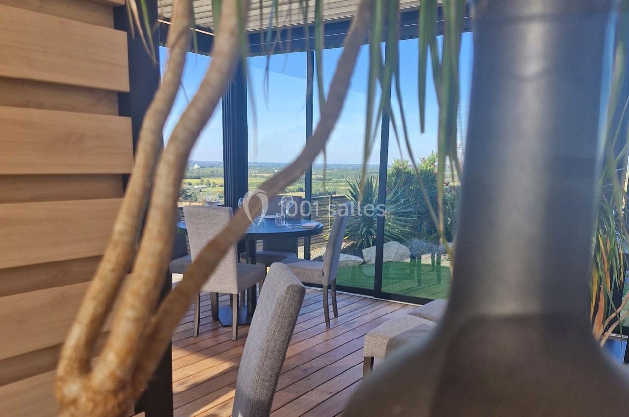 Vue d'une terrasse ensoleillée avec table dressée, entourée de plantes et offrant un panorama sur la campagne.