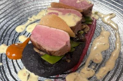 Plat gastronomique composé de viande, légumes, champignons, sauce caramélisée et croustillant sur une assiette décorative.