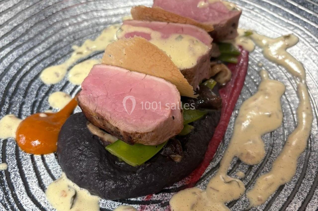 Tranche de viande rosée sur purée noire, légumes verts, sauce crémeuse et touche de purée orange.