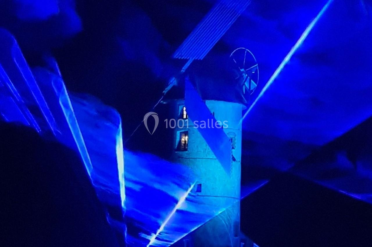 Un moulin éclairé par des lumières bleues dans une ambiance nocturne avec des effets lumineux.