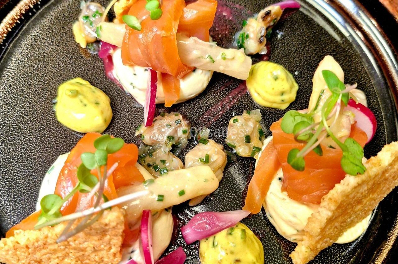 Assiette gastronomique avec saumon fumé, légumes marinés, herbes fraîches, crème et croustillants sur une assiette noire.