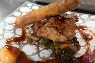 Plat gastronomique composé de viande, légumes, champignons, sauce caramélisée et croustillant sur une assiette décorative.