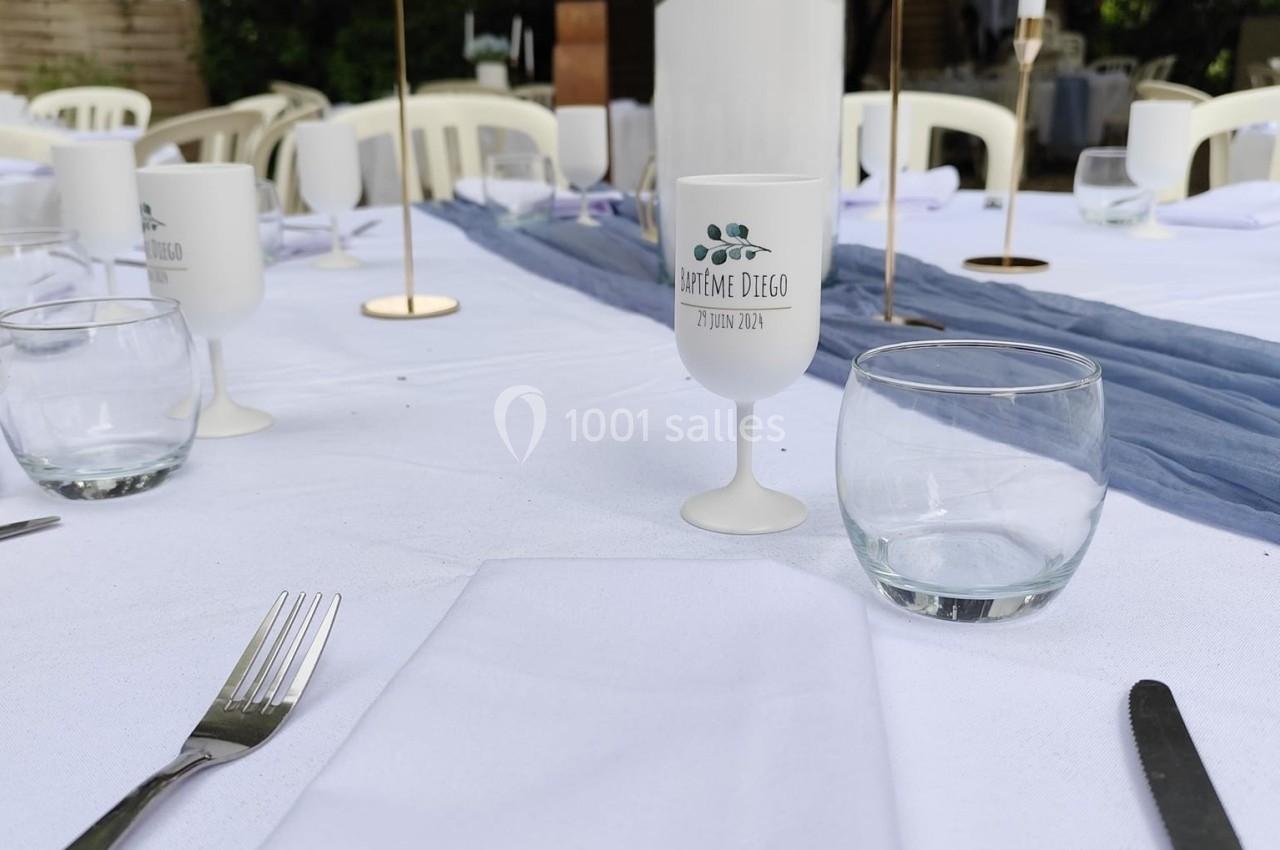 Table dressée en extérieur avec nappes blanches, verres, couverts, bougies et centre de table floral.