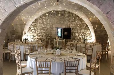 Salle de réception avec tables rondes dressées, nappes blanches, chemins de table en dentelle et décoration élégante.