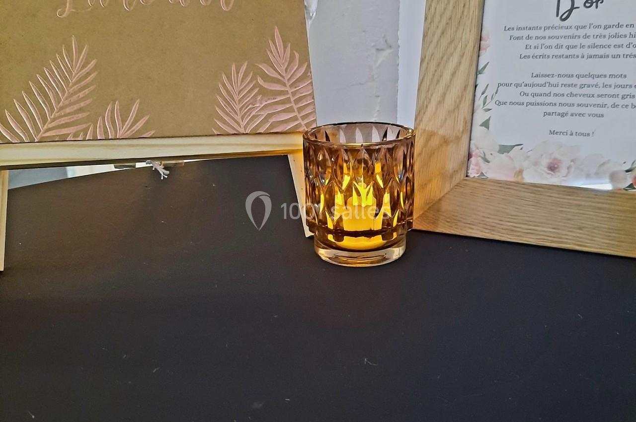 Livre d'or décoratif sur un chevalet, bougie ambrée allumée et cadre en bois sur une table noire.