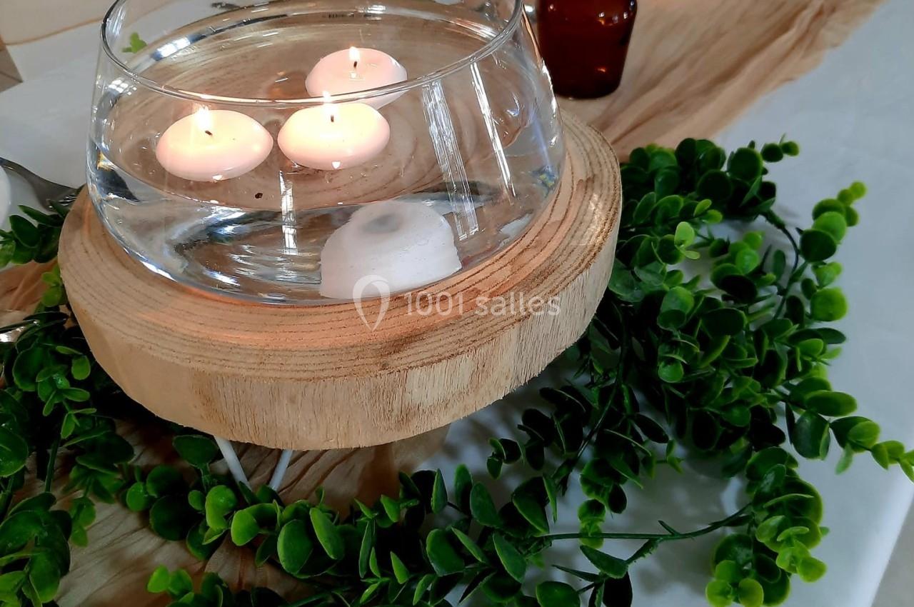 Bougies flottantes dans un vase en verre sur support en bois, entouré de feuillage et décorations de table.