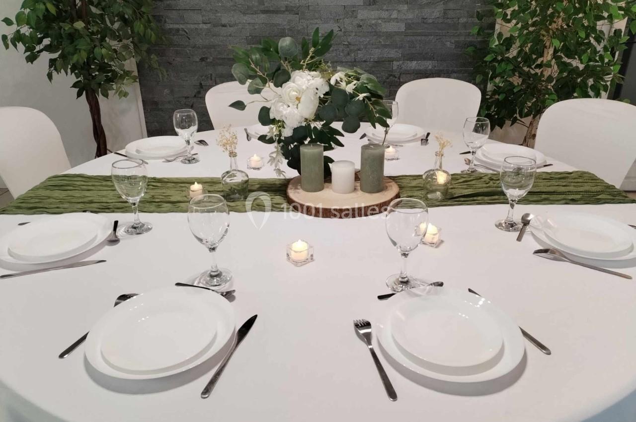 Table ronde élégamment dressée avec nappe blanche, chemin de table vert, bougies, vaisselle et centre de table floral.