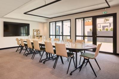 Salle à manger lumineuse avec une grande table en bois, des chaises en rotin et des étagères décoratives en arrière-plan.