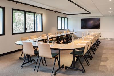 Salle à manger lumineuse avec une grande table en bois, des chaises en rotin et des étagères décoratives en arrière-plan.