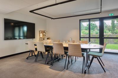 Salle à manger lumineuse avec une grande table en bois, des chaises en rotin et des étagères décoratives en arrière-plan.