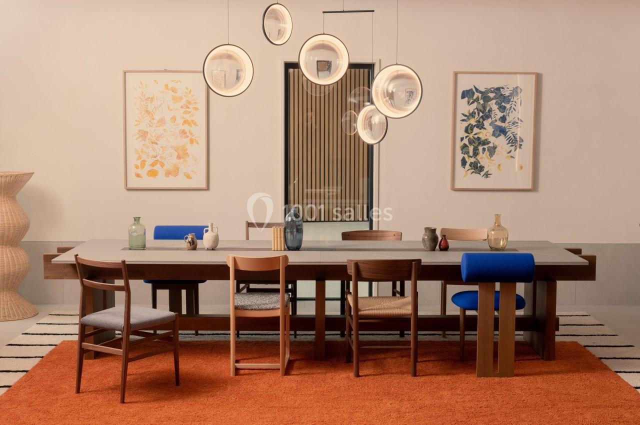 Salle à manger avec table en bois, chaises variées, suspension lumineuse moderne et décorations murales colorées.