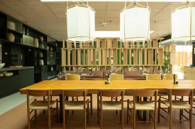 Salle à manger lumineuse avec une grande table en bois, des chaises en rotin et des étagères décoratives en arrière-plan.