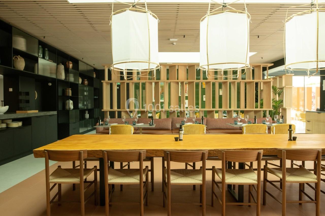 Salle à manger lumineuse avec une grande table en bois, des chaises en rotin et des étagères décoratives en arrière-plan.