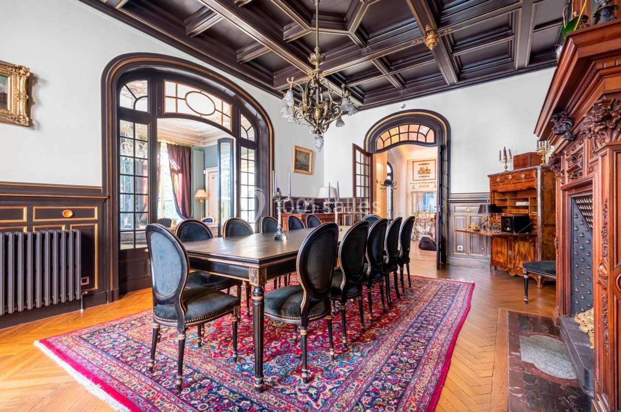 Salle à manger élégante avec table en bois, chaises noires, tapis rouge, moulures sombres et lustre central.