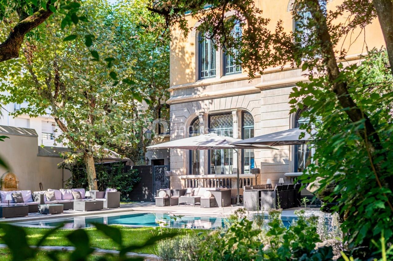 Jardin avec piscine, mobilier de terrasse et parasols devant une façade élégante entourée de végétation.