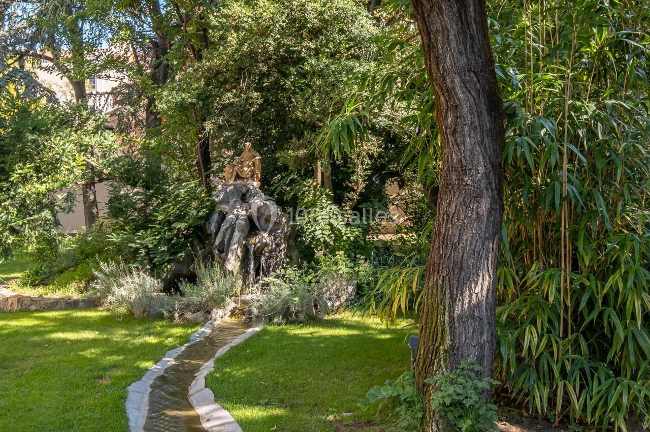 Un petit canal sinueux traverse une pelouse verdoyante, entouré d'arbres et de bambous dans un jardin paisible.