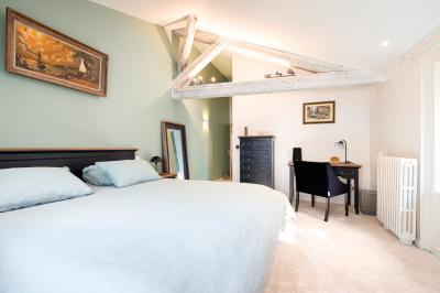 Chambre lumineuse avec lit double, bureau, poutres apparentes et murs verts, décorée avec des tableaux.