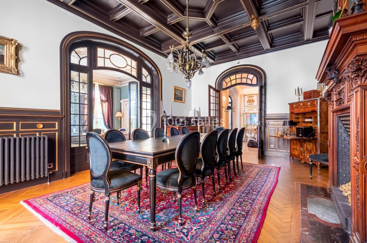 Salle à manger élégante avec table en bois, chaises noires, tapis rouge et plafond à caissons sombres.