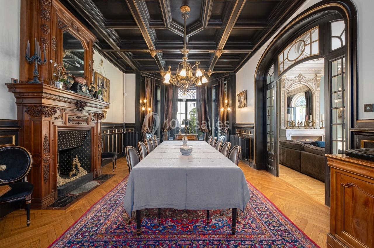 Salle à manger élégante avec table dressée, cheminée en bois sculpté, lustre et parquet en chevrons.
