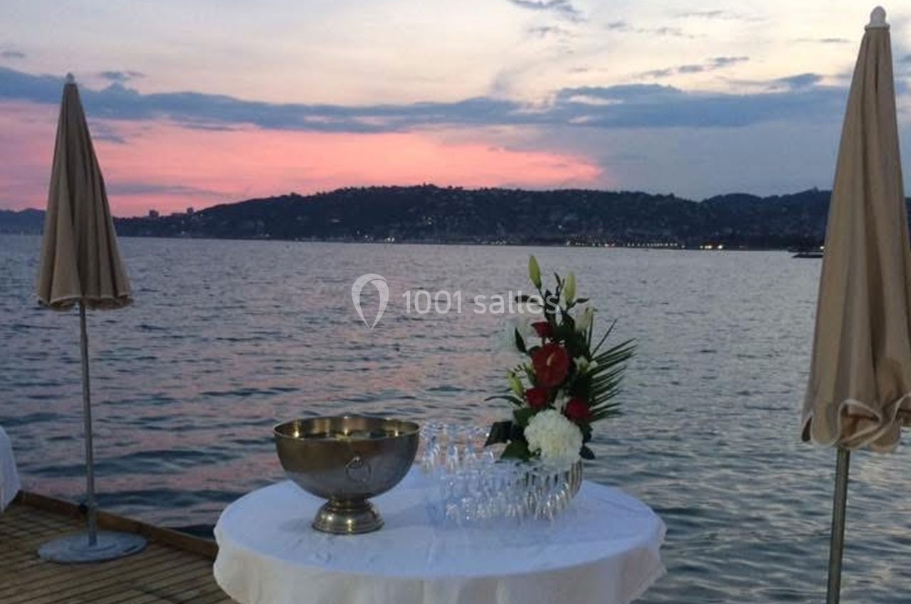 Table dressée avec un seau à champagne, des verres et un bouquet, sur un ponton au bord de l'eau au coucher du soleil.