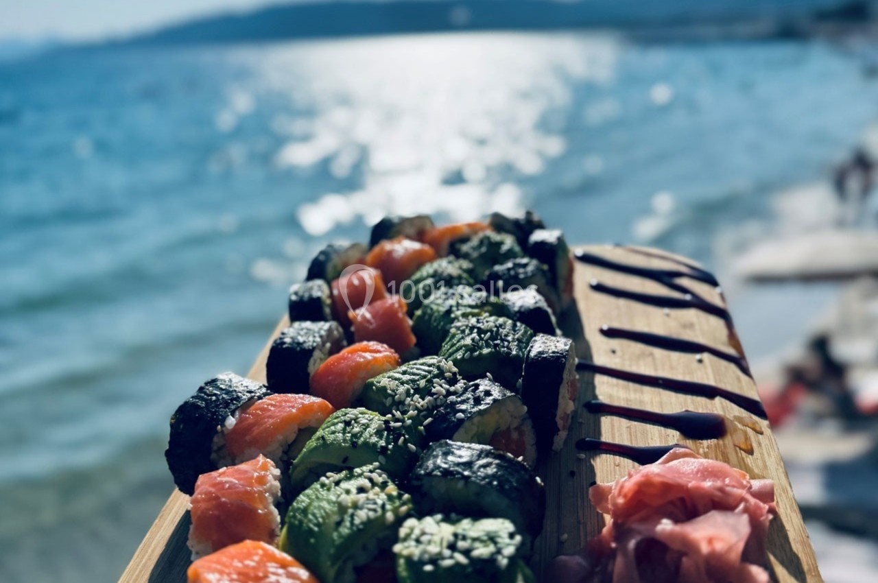Plateau de sushis variés avec gingembre mariné, présenté sur une planche en bois, en bord de mer ensoleillé.