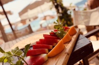 Plateau en bois avec verrines garnies de crevettes, tomates, olives et herbes fraîches, disposées sur une nappe beige.