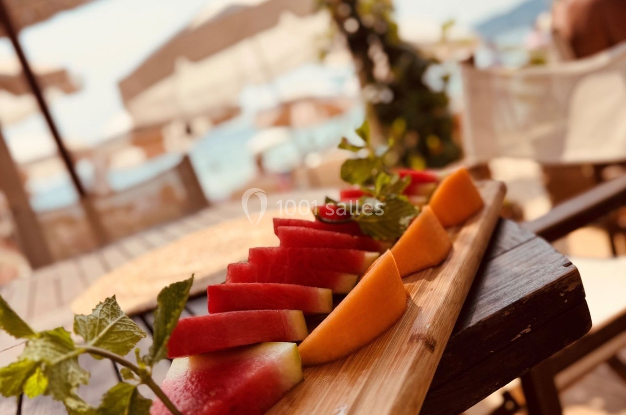 Tranches de pastèque et de melon disposées sur une planche en bois, avec un décor estival en arrière-plan.