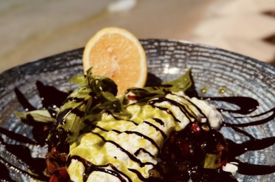 Plateau en bois avec verrines garnies de crevettes, tomates, olives et herbes fraîches, disposées sur une nappe beige.